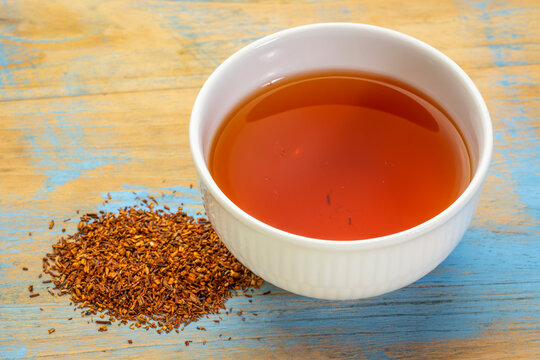 rooibos red tea  -  a white cup of a hot drink and loose leaves on grunge wood background, tea made from the South African red bush, naturally caffeine free