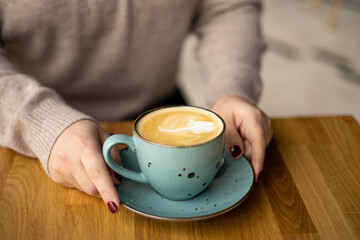 Womans Hands holding a cup of coffee over table. Still life with cup of latte. Coffee in ceramic blue cup on wooden table in cafe