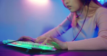 Close up hand of gamer playing cyber video game online with personal computer keyboard at home, woman actively pushing gaming keyboard buttons in the neon room
