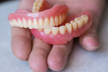 hand holding dentures. Dentures are realistic, with natural colors of teeth and gums