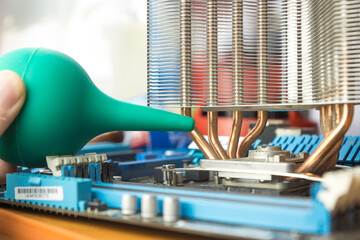A close-up view of a maintenance process where a technician utilizes a manual air blower to remove dust from a desktop computers metal heat sink.