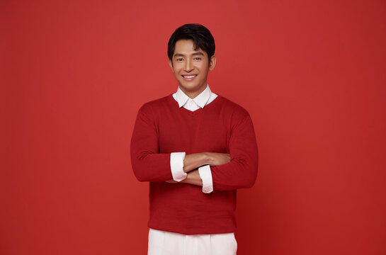 Portrait of attractive young southeast Asian man standing with crossed arms isolated on red background.