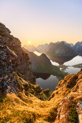 The midnight sun casts a warm glow over the moss-covered rocks of Reinebringen, with a view overlooking the Lofoten Islands  the serene Reinefjorden reflects the mountainous. Norway