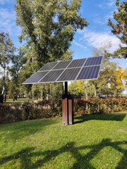 An installation with solar panels is installed in a city park on the grass to illuminate the park with lamps at night