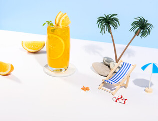 Glass of 100% Orange juice with orange slices fruits on sea beach with white sand. Summer sea vacation and travel concept. Exotic summer drinks.