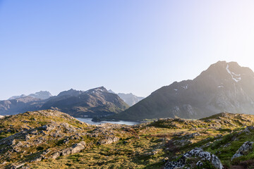 The sun casts a golden glow over a rugged landscape, highlighting the textured terrain and distant...