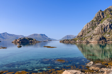 The calm waters of the Norwegian Sea gently lap against Lofoten's rocky coastline, with majestic...