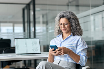 Busy middle aged business woman holding cell mobile phone using cellphone in office. Mature...