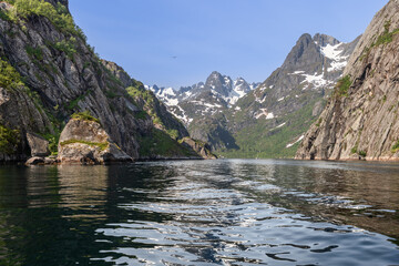 Fototapeta premium Jagged cliffs and snow-laden mountain peaks rise above Trollfjorden's dark waters, as a bird soars under the expansive Norwegian sky