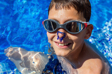Little boy in the pool with nose clip and goggles. Summer break vacation.