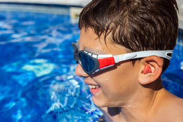 Little boy getting ready to swim in the pool, having ear plugs and goggles. Summer break vacation.