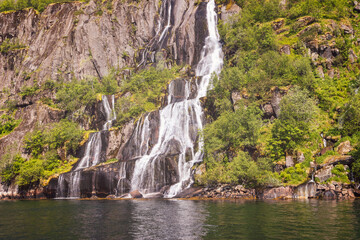 Fototapeta na wymiar A vintage-toned photo captures a majestic waterfall cascading into Trollfjorden, Lofoten, Norway, surrounded by lush greenery and sun-kissed cliffs