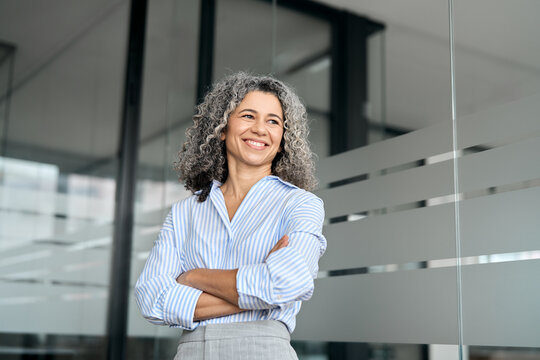 Happy mature business woman leader standing in office looking away. Smiling confident older middle aged professional lady corporate leader, senior female executive or entrepreneur portrait.
