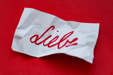 liebe - Botschaften mit Handschrift auf einem Zettel, der zerknüllt auf einem roten Karton liegt