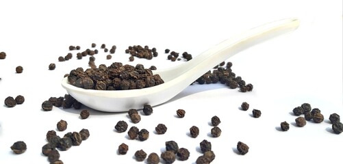 Black pepper in spoon isolated in white background. Spoon and black peppercorn composition over a...