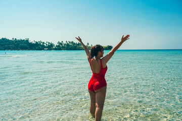 Beautiful Woman in the Sea Waves Rear View. Woman arms rised, wearing bikini, happy, enjoying amazing view on Koh Kood Island, Thailand. Summer vacations on picture perfect tropical beach concept.