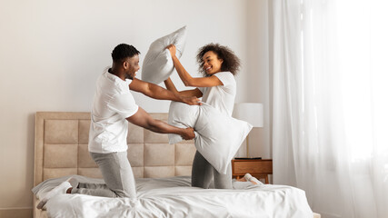 African American spouses having pillow battle for fun at bedroom