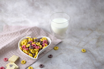 sweet multi-colored cereal rings for a healthy breakfast in a heart-shaped plate, milk in a transparent double-walled mug.selective focus.