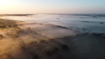 Fototapeta na wymiar Aerial drone view of meadow landscape in The Netherlands on a sunny, foggy morning. Misty low clouds farmland landscape captured from above.