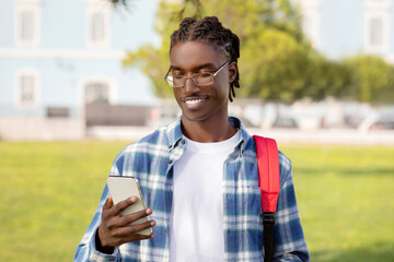 African student man holding smartphone, scrolls through educational app outdoors