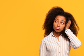 Pensive black woman with hand in hair on yellow background - obrazy, fototapety, plakaty