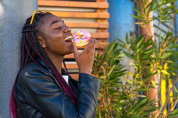 Cheerful African woman biting a doughnut outdoors