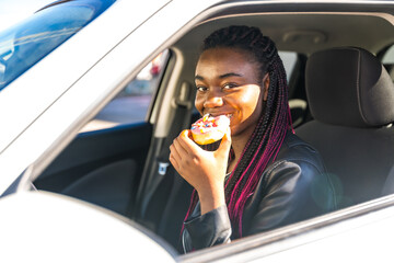 Naklejka premium Cheerful african woman biting a doughnut sitting in a car