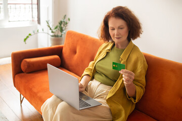 Online Shopping. Smiling Senior Woman Using Laptop And Credit Card At Home