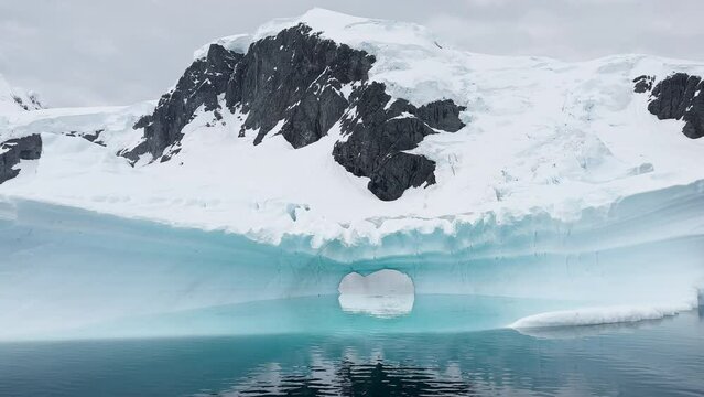 Arch in a huge iceberg, high breakaway glacier drifts in the southern ocean off the coast of Antarctica at sunset, the Antarctic Peninsula, the Southern Arctic Circle, azure water, cloudy weather