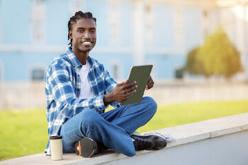 black guy student sitting with digital tablet outdoors in park
