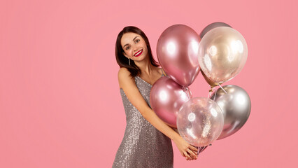 Smiling woman in a glamorous sequin dress holding a cluster of metallic and transparent balloons