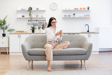 Happy young woman working remotely from home, typing on modern wireless cell phone. Relaxed lady...