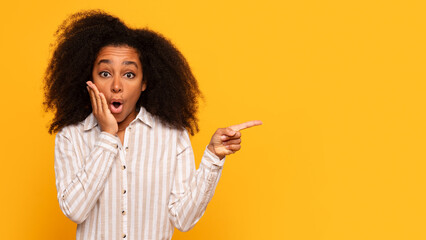 Shocked black woman pointing to side on yellow background