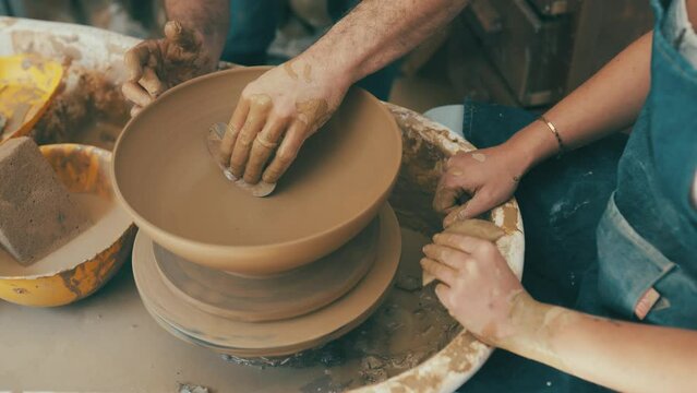 People, hands and clay on spinning table in pottery for bowl, vase or ceramics in creativity, art or shape at workshop. Closeup of sculptor, team or artist working with mold for crafting in startup