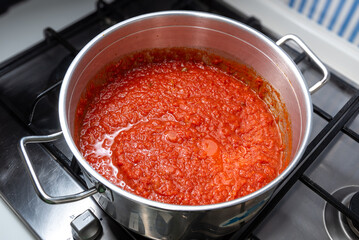 Neapolitan-style red tomato sauce cooks in a pot on a hob, top view. Tomato ragout meat in a steel pot