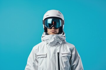 A male skier or snowboarder in a white jacket, helmet and ski goggles. An isolated studio photograph of a man on a blue background.