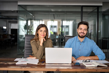 Happy confident professional mature business woman and young business man corporate managers colleagues sitting in office with laptop, two diverse colleagues executives team together, portrait. - obrazy, fototapety, plakaty