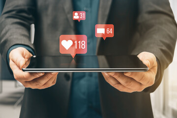 Close up of businessman hands holding tablet with creative social media icons hologram on blurry office interior background. Community, likes, shares and communication concept.