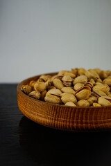 a lot of pistachios lie in a wooden plate on a black surface on a white background
