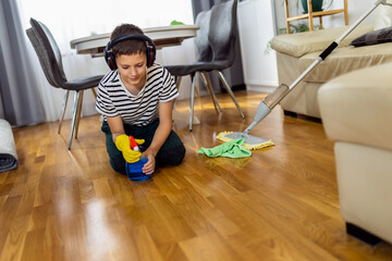 Male kid cleaning the floor with cloth while wearing the headphones and listening to the music