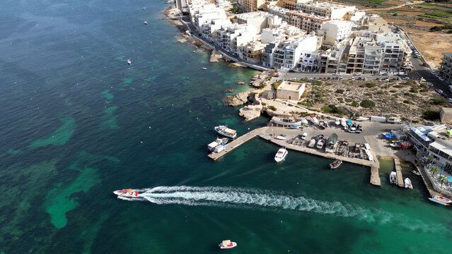 Aerial view of speedboat leaving Mellieha harbor with trail behind in clear turquoise Mediterranean sea. 
