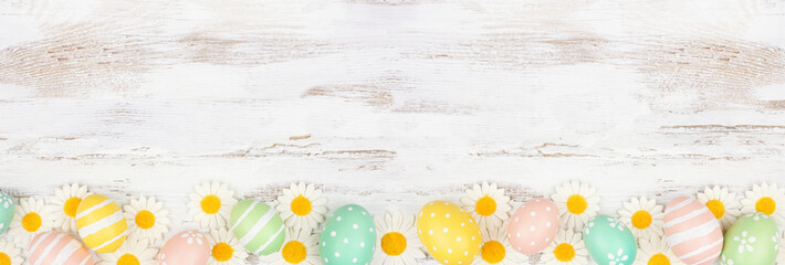 Easter eggs and white daisy flowers. Top view bottom border against a rustic white wood banner...