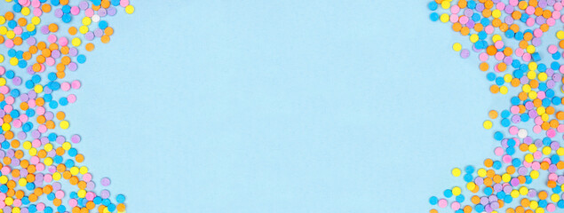 Colorful candy sprinkles double border. Overhead view on a blue banner background. Pastel Easter color theme. Copy space.