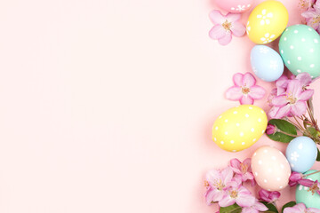 Easter eggs and cherry blossom flowers. Top view side border against a soft pink background. Copy space.