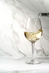 Studio shot of a white wine glass being filled, isolated on a white marble background