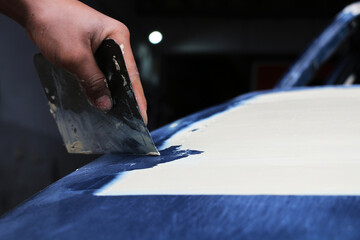 Mechanic repairs car body by sanding primer before painting and puttying after accident.