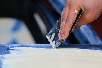 Mechanic repairs car body by sanding primer before painting and puttying after accident.