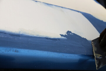 Mechanic repairs car body by sanding primer before painting and puttying after accident.
