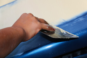 Mechanic repairs car body by sanding primer before painting and puttying after accident.