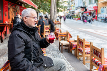 Male tourist drinking a pomegranate juice for refreshment. Portrait face of thirsty  mature solo hipster traveler holding a pomegranate drink on street.